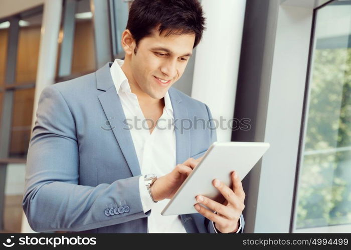 Businessman standing with tablet smiling at camera. Success and professionalism in person