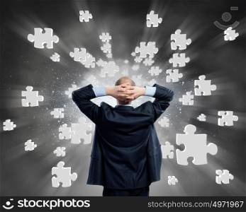 Businessman stands back and looks at flying objects. Businessman and flying puzzle