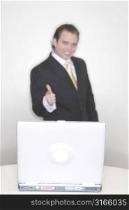 Businessman stands behind his laptop and points his finger in confidence
