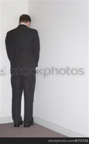 Businessman stands in the corner against a white wall in the office
