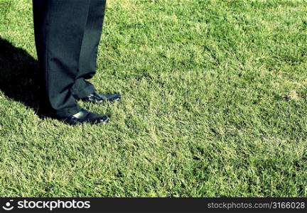 Businessman stands in the grass with his business shoes outside