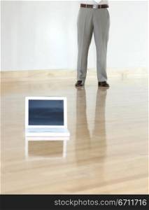 Businessman stands next to his white laptop, which is place in the middle of a wooden floor