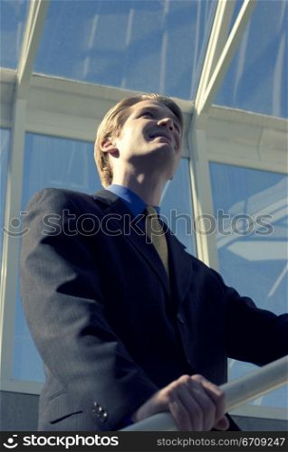 Businessman stands on the railing and looks up with vision
