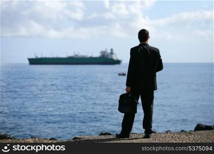 Businessman staring at a tanker out at sea