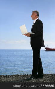 Businessman stood holding a laptop at the beach