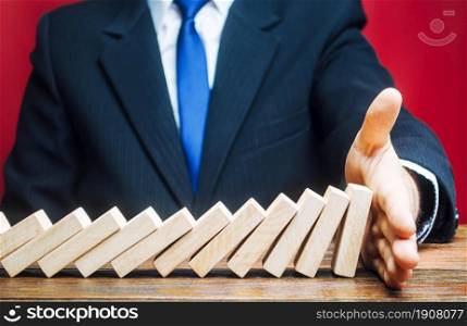 Businessman stops domino falling with his palm. Risk management concept. Successful strong business and problem solving. Stop the destructive processes. Strategy development. Debt restructuring