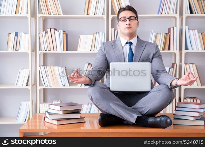 Businessman student in lotus position meditating with a laptop i. Businessman student in lotus position meditating with a laptop in library