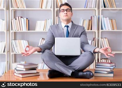 Businessman student in lotus position meditating with a laptop i. Businessman student in lotus position meditating with a laptop in library