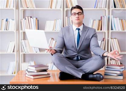 Businessman student in lotus position meditating with a laptop i. Businessman student in lotus position meditating with a laptop in library