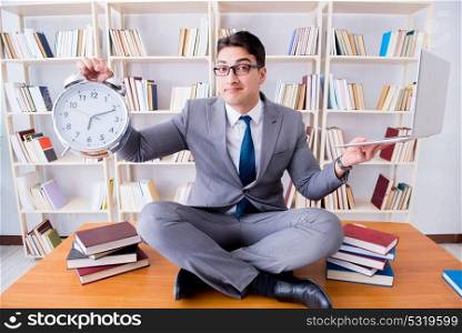 Businessman student in lotus position with an alarm clock and a . Businessman student in lotus position with an alarm clock and a laptop in library