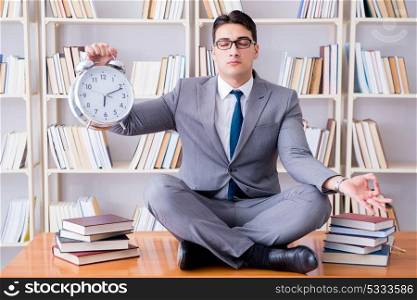 Businessman student in lotus position with an alarm clock in lib. Businessman student in lotus position with an alarm clock in library