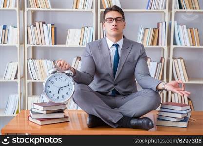 Businessman student in lotus position with an alarm clock in lib. Businessman student in lotus position with an alarm clock in library