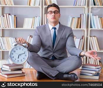 Businessman student in lotus position with an alarm clock in library. Businessman student in lotus position with an alarm clock in lib