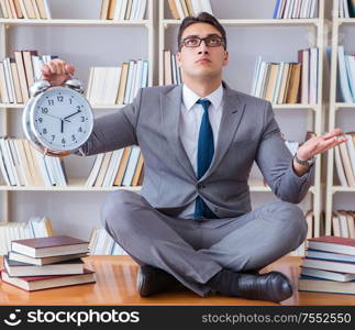 Businessman student in lotus position with an alarm clock in library. Businessman student in lotus position with an alarm clock in lib