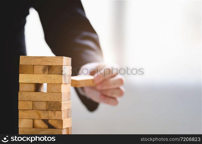 Businessman take and picking one wood block on stacked tower by hand as startup project. Business organization and company growth progress. Success of strategy and money investment. Risk management