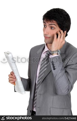 Businessman taking on phone and holding newspaper
