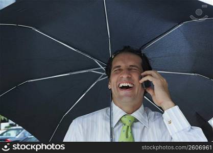 Businessman talking on a mobile phone and laughing under an umbrella
