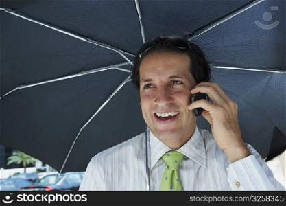 Businessman talking on a mobile phone and smiling under an umbrella