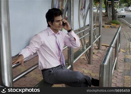 Businessman talking on a mobile phone at a bus stop