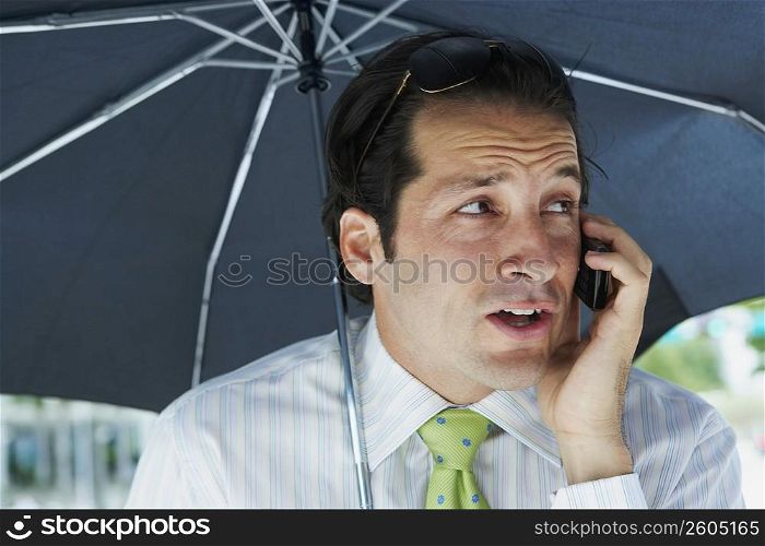 Businessman talking on a mobile phone under an umbrella