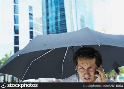 Businessman talking on a mobile phone under an umbrella