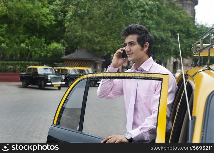 Businessman talking on a mobile phone while getting out of a taxi