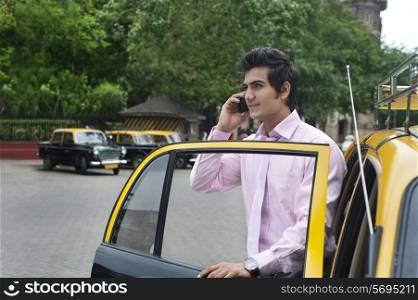 Businessman talking on a mobile phone while getting out of a taxi