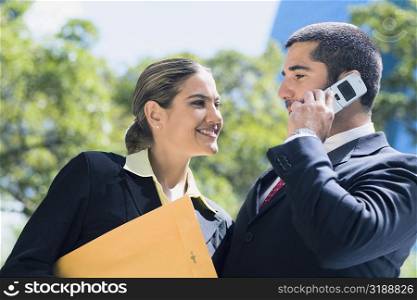 Businessman talking on a mobile phone with a businesswoman smiling beside him