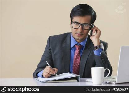 Businessman talking on mobile phone and making notes at desk