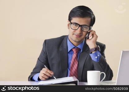 Businessman talking on mobile phone and making notes at desk