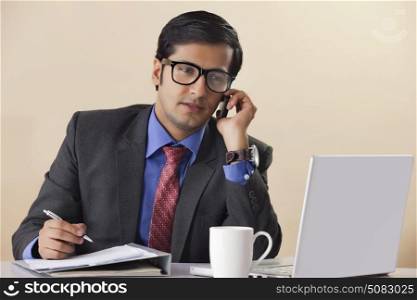Businessman talking on mobile phone at computer desk