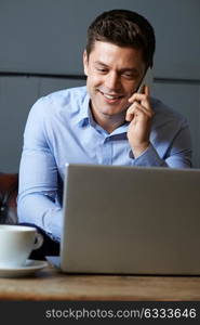 Businessman Talking On Mobile Phone Working On Laptop In Internet Cafe