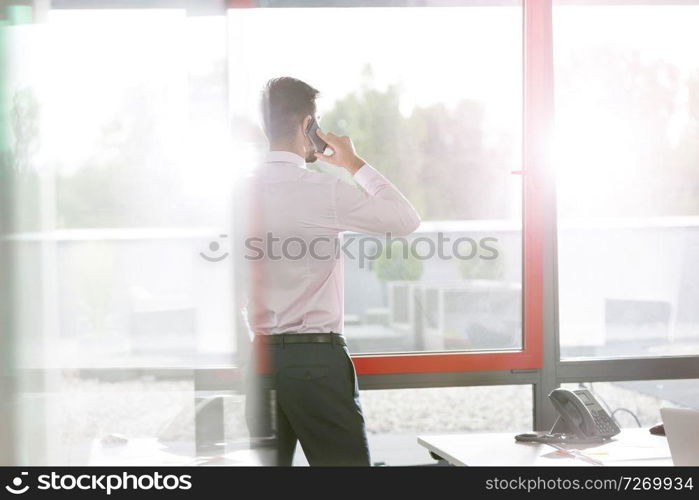 Businessman talking on smartphone by window at office desk