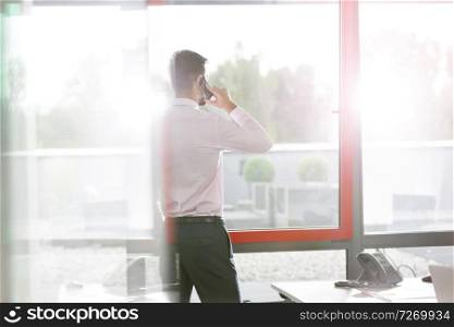 Businessman talking on smartphone by window at office desk
