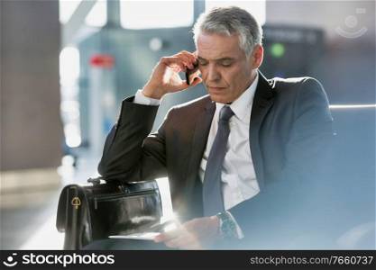 Businessman talking on smartphone while sitting and waiting in his gate for boarding in airport