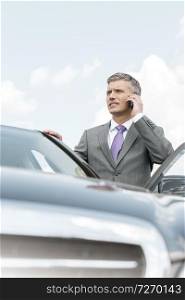Businessman talking on smartphone while standing outside car
