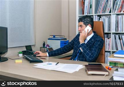 Businessman talking on smartphone while working with computer at workplace. Businessman talking on smartphone and working with computer
