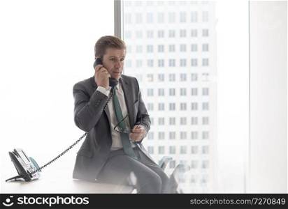 Businessman talking on telephone while sitting on desk in office