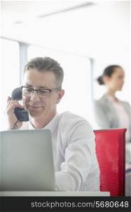 Businessman talking on telephone with colleague in background at office