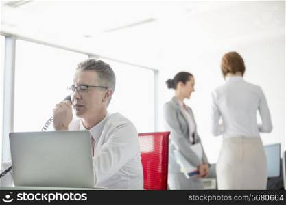 Businessman talking on telephone with colleagues in background at office