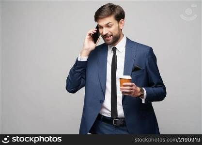 businessman talking on the phone and holding cup of coffee isolated over grey background in studio shooting. businessman talking on the phone and holding cup of coffee isolated over grey background