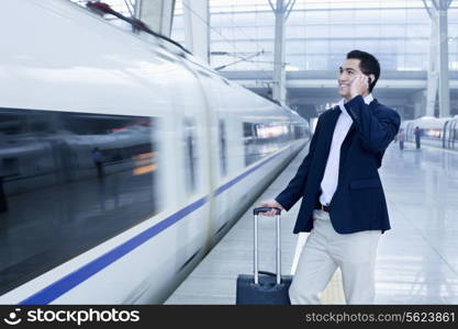 Businessman talking on the phone on the railroad platform by a high speed train in Beijing