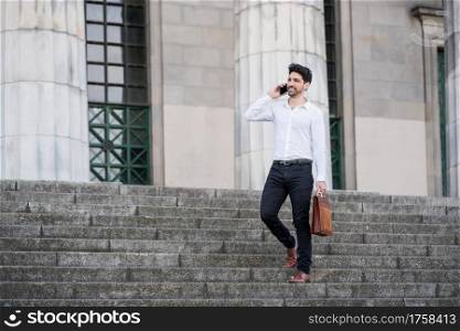 Businessman talking on the phone while standing on stairs outdoors. Business concept.