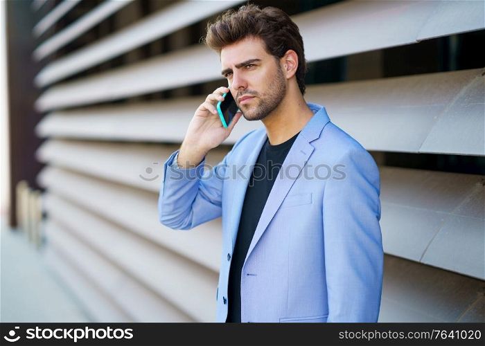 Businessman talking to his smartphone wearing blue suit outdoors.. Businessman talking to his smartphone wearing blue suit.