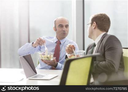 Businessman talking with colleague while eating lunch in boardroom during meeting at office