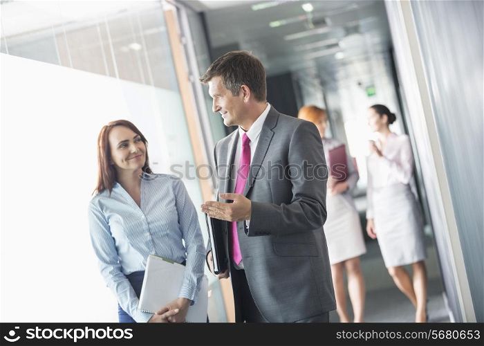 Businessman talking with female colleague while walking in office corridor