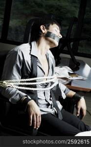 Businessman tied with rope on a chair in an office