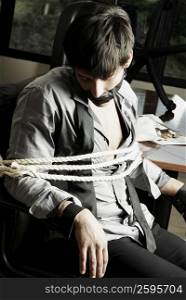 Businessman tied with rope on a chair in an office