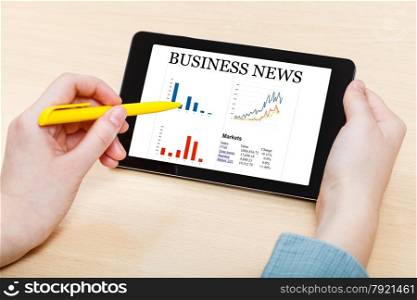 businessman touches by pen of tablet PC with business news on screen at office desk