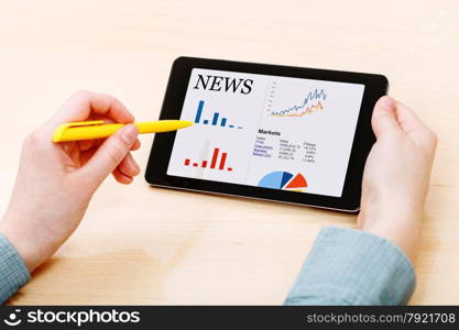 businessman touches by pen of tablet PC with business news on screen at office table